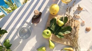 Una mesa con una botella de miel, un vaso de agua, un vaso de vino blanco, un limón y algunas peras sobre un mantel blanco.