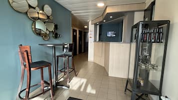 Un hall d’hôtel comprenant un comptoir d’accueil, un bar avec des tabourets et une vitrine exposant des bouteilles.