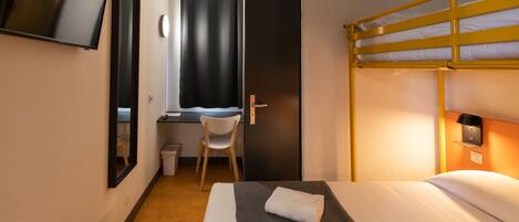 Une chambre d’hôtel avec un lit superposé, un bureau avec une chaise, une télévision et une fenêtre avec des rideaux.