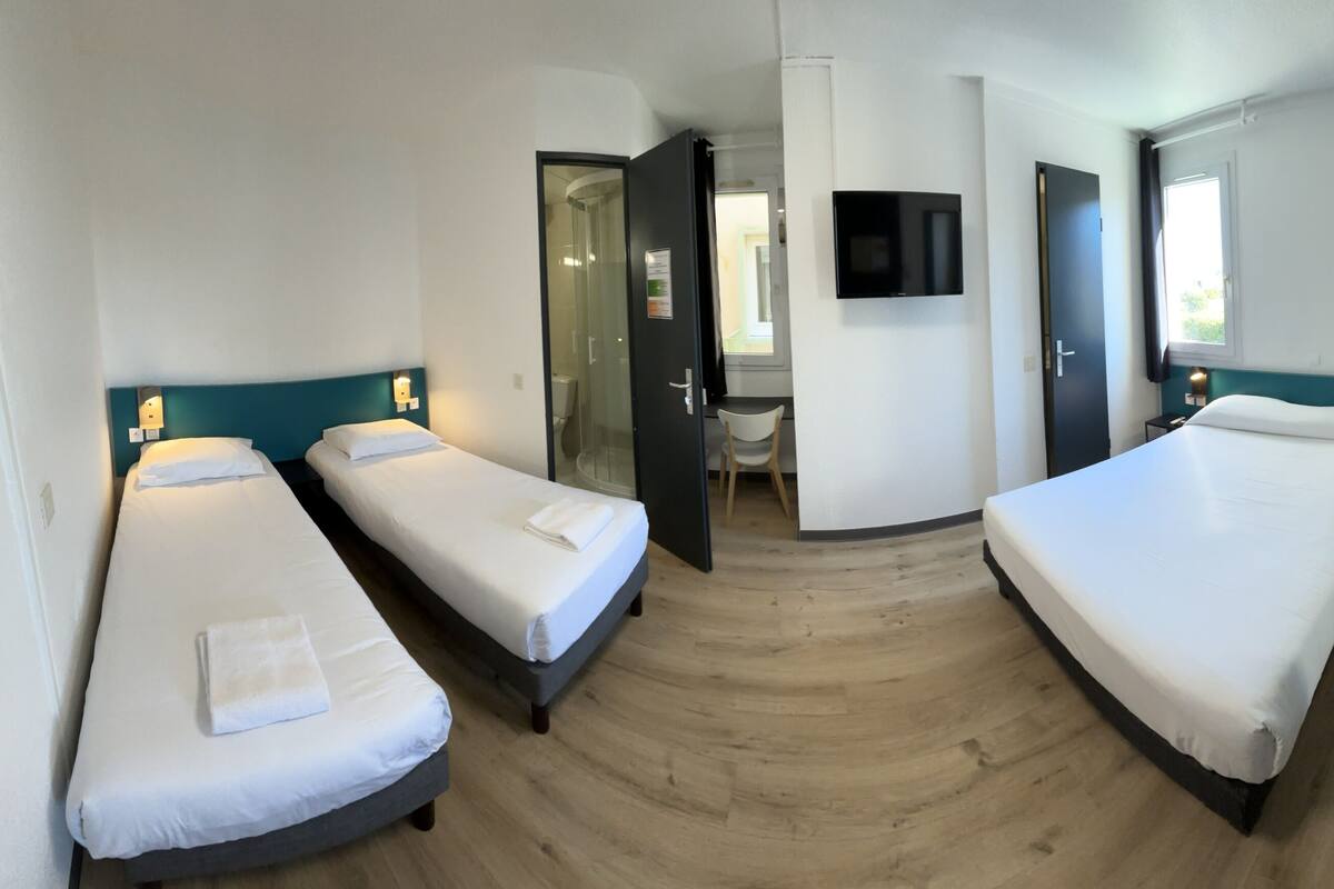 A hotel room with three single beds, a TV, a desk, and a wardrobe.
