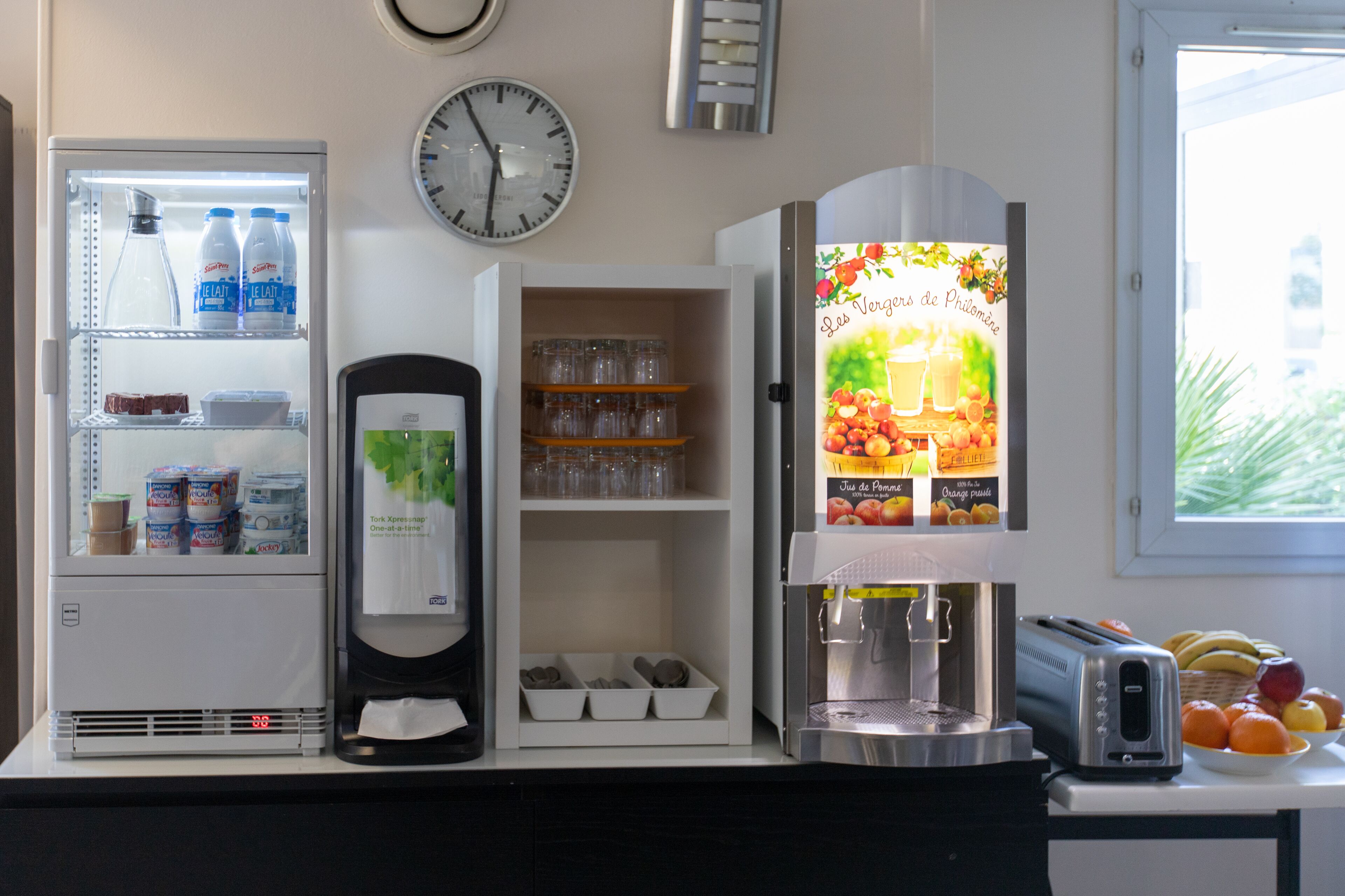 A kitchen with a refrigerator, a coffee machine, a toaster, and a window with a view of greenery.