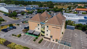 A hotel with a parking lot, a road in the background, and a building with a sign that reads "hotel AKENA". - Hôtel Face West Le Pontet (Le Pontet)