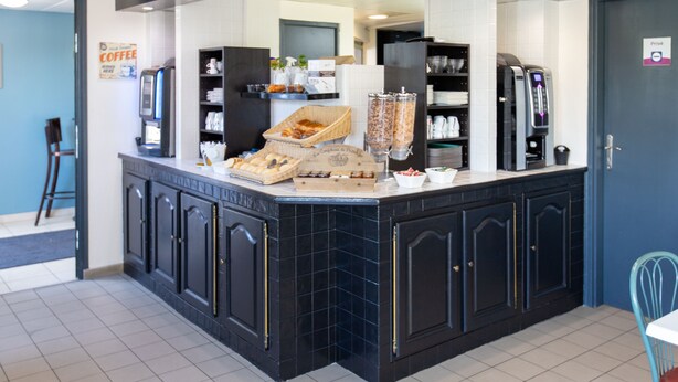 A self-service breakfast bar with a variety of food items, a coffee machine, and a seating area with a chair. - Hôtel Face West Le Pontet (Le Pontet)