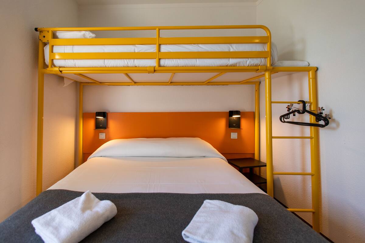 A bunk bed with a ladder, a bedside table, and two wall-mounted lamps.