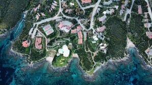 Vista aerea di una località balneare con diversi edifici, una piscina centrale e paesaggi naturali circostanti.