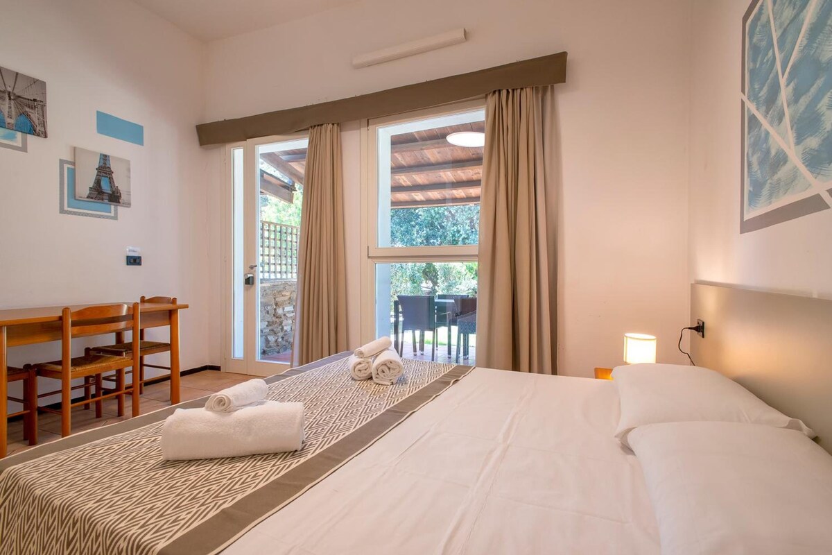Une chambre d’hôtel avec un lit, un bureau et une chaise. Il y a une fenêtre avec des rideaux, et la vue donne sur l’extérieur.