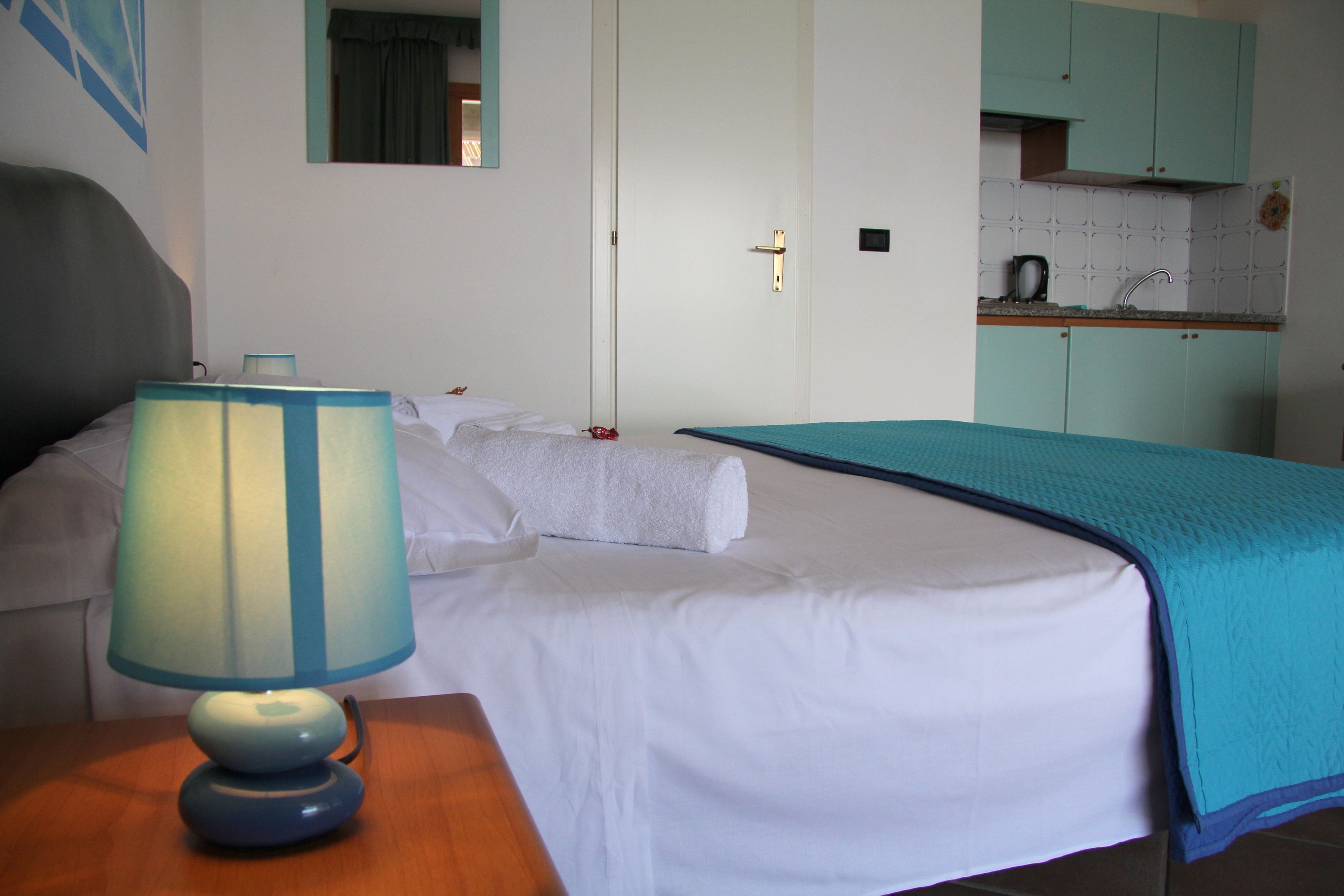 Een hotelkamer met een bed, een bedlampje, een klein tafeltje, een kitchenette en een badkamers deur.