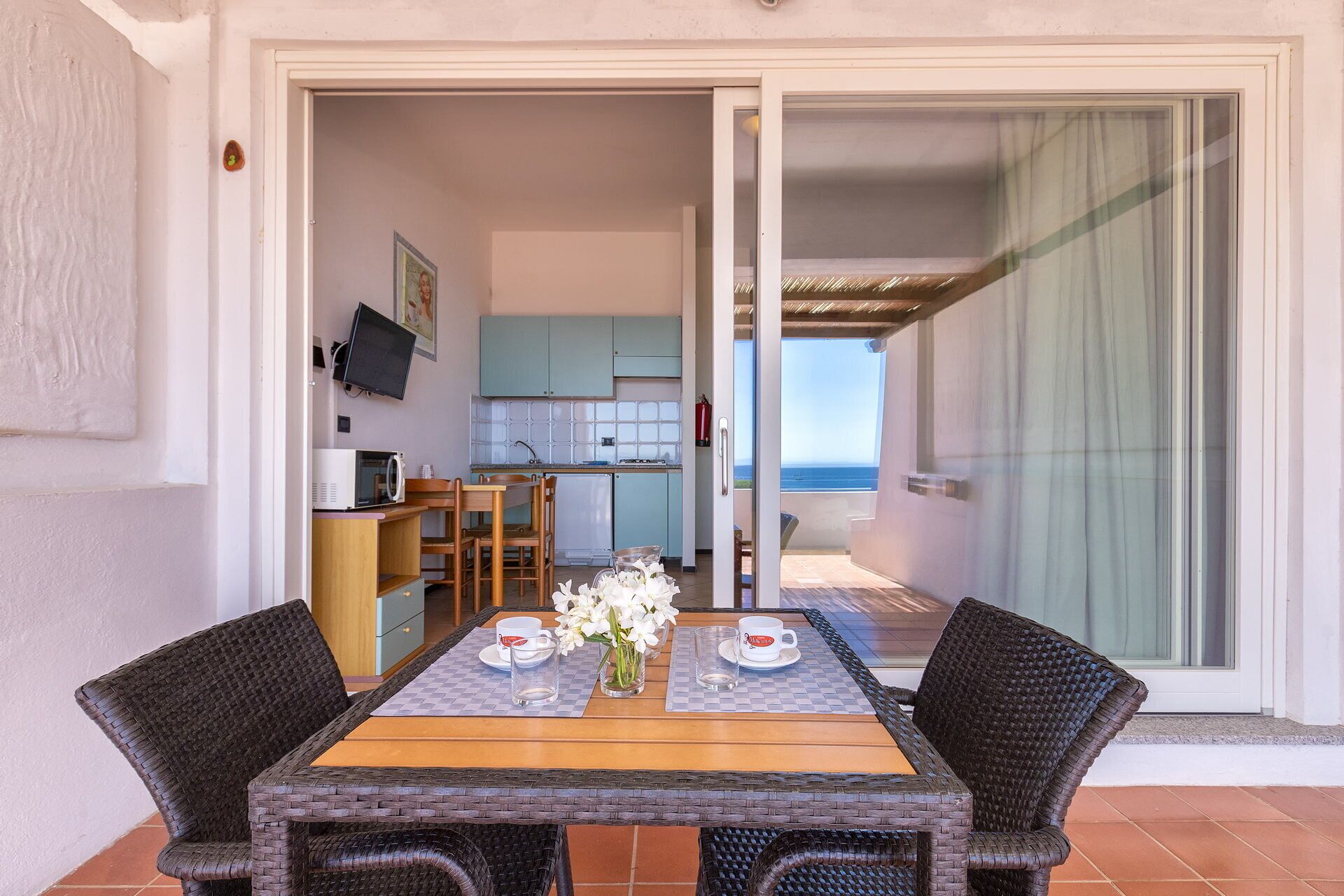 Zona pranzo con tavolo e sedie, cucina sullo sfondo e vista sul mare tramite una porta scorrevole.