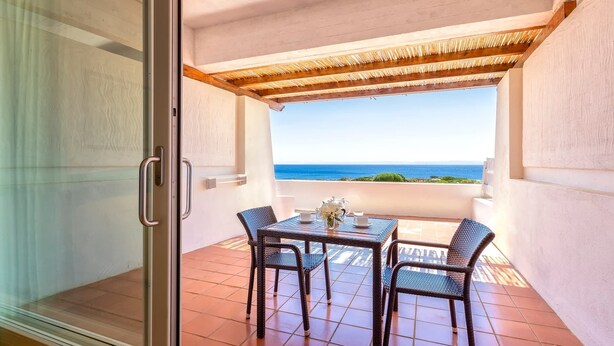 Un balcone con tavolo e sedie, vista sul mare e tetto di paglia.