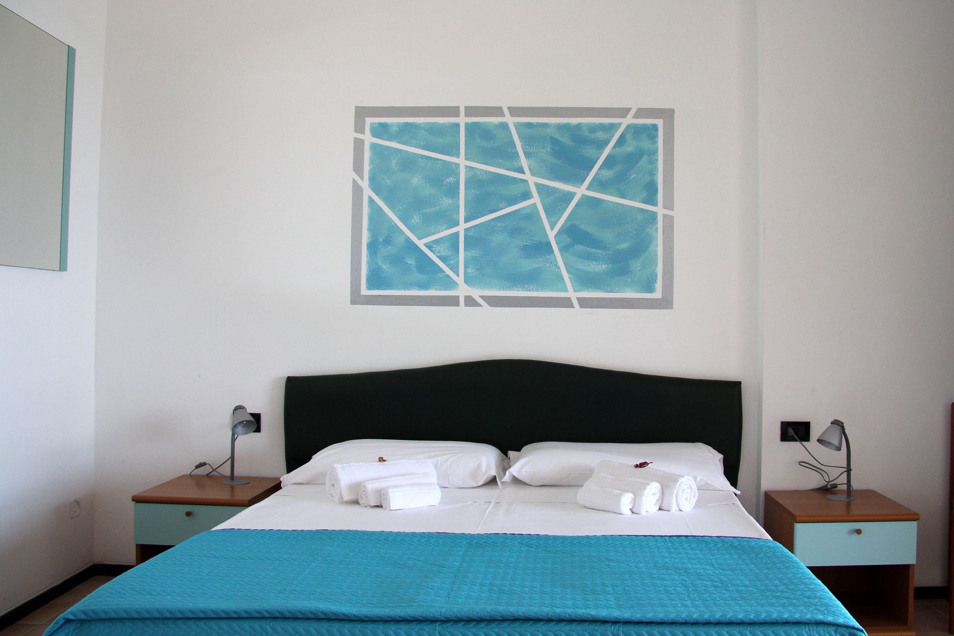 Ein Hotelzimmer mit einem Bett, zwei Nachttischen, einem Wandbild und einer blauen Bettdecke.