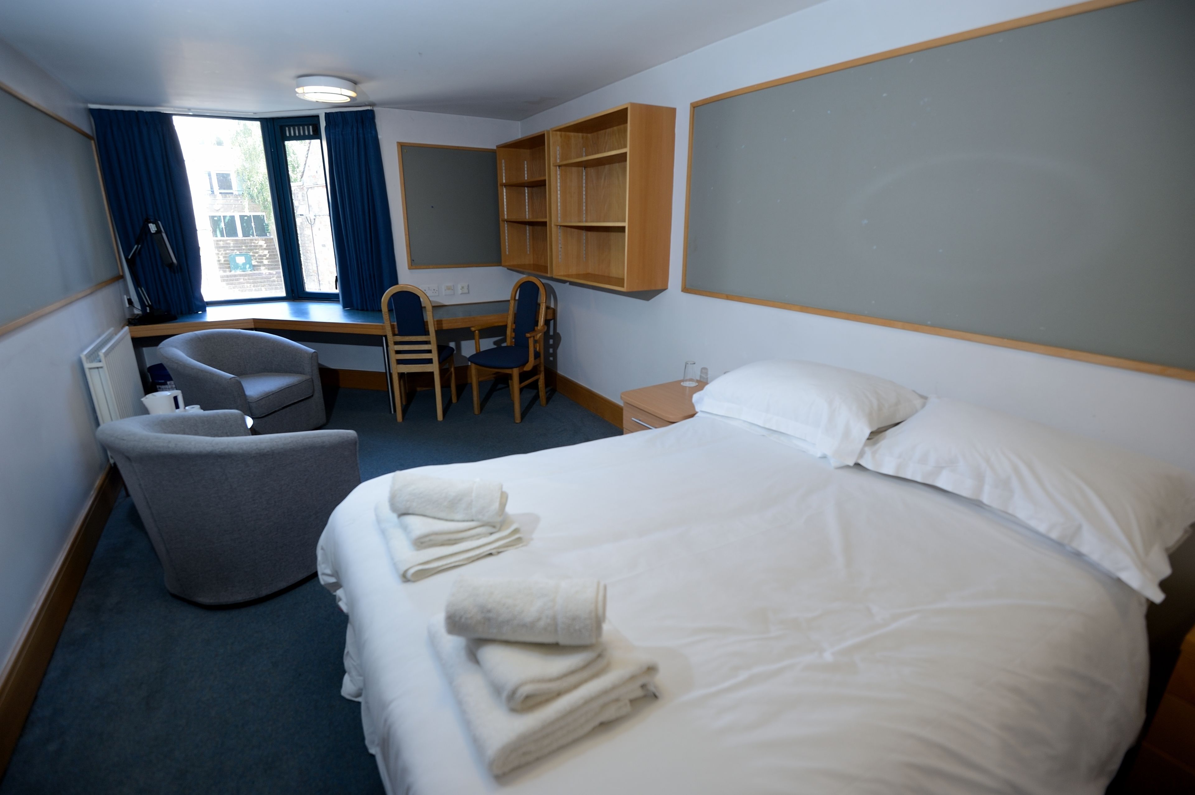 A hotel room with a bed, a desk, two chairs, a small table, and a window with curtains.