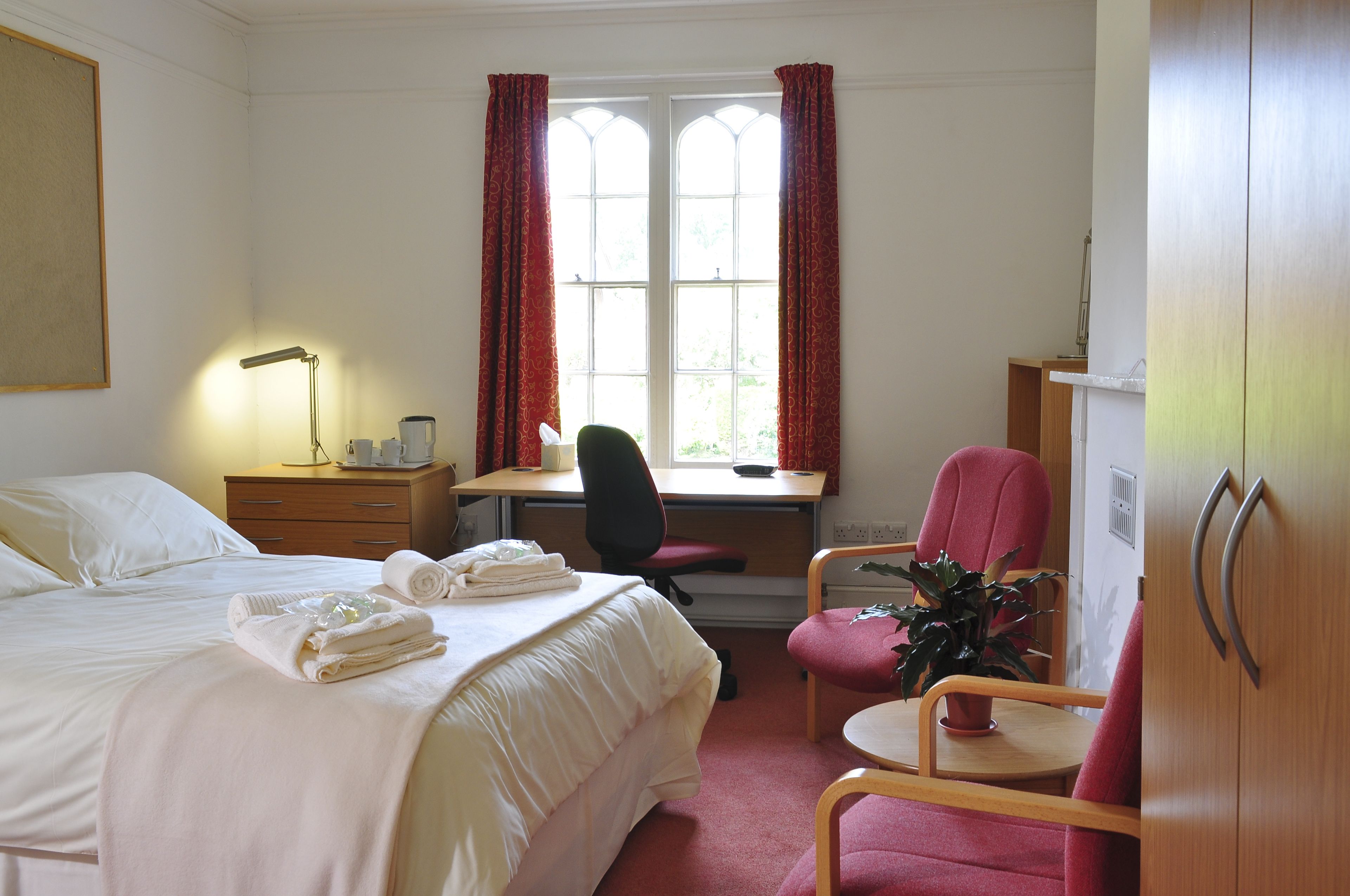 A hotel room with a bed, desk, chair, and wardrobe.