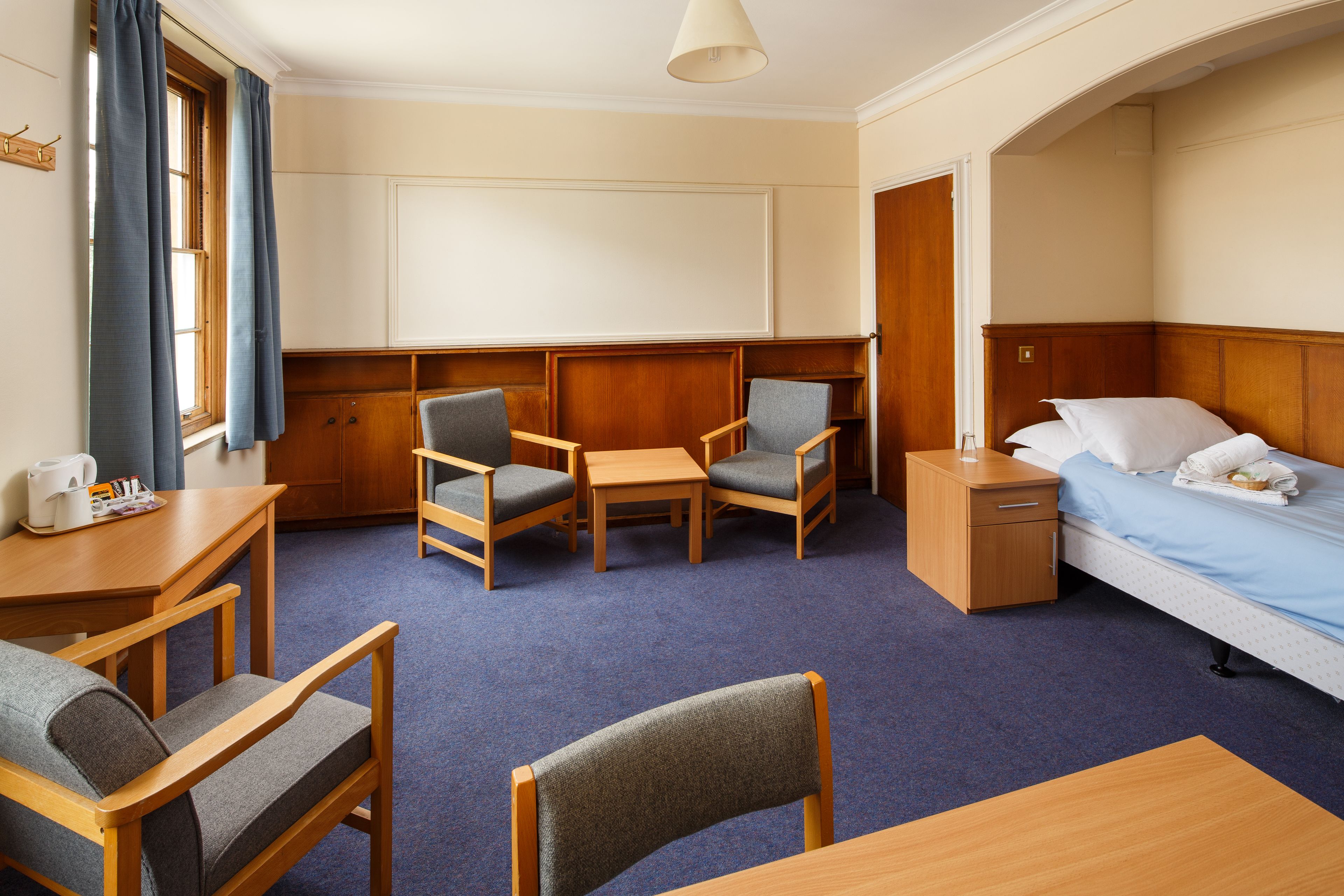 A hotel room with a bed, two armchairs, a table, a nightstand, and a window with curtains.