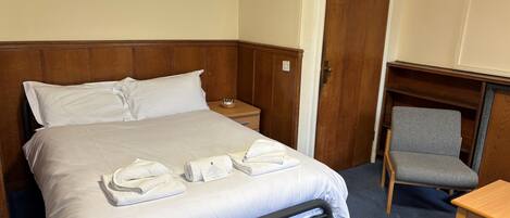 A hotel room with a bed, a chair, a small table, and a wooden wardrobe.