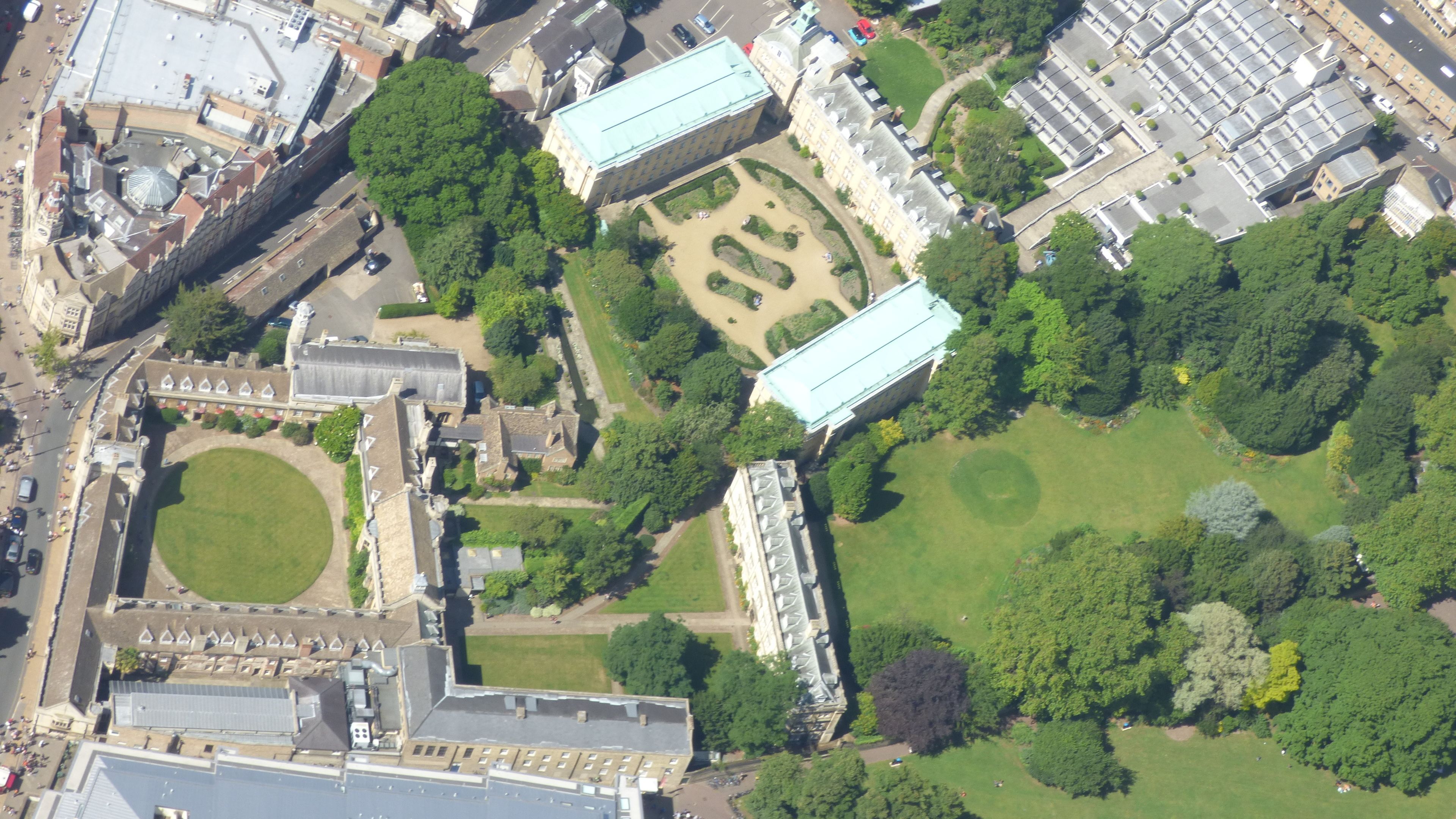 An aerial view of a historic building complex with multiple structures, including a large central building with a dome, surrounded by smaller buildings and green spaces.