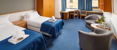 A hotel room with two beds, a desk, a chair, and a small table with a plant.