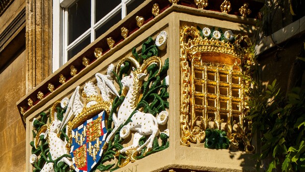A building facade with ornate gold detailing, a coat of arms, and a wooden door. - Christs College Cambridge (Cambridge)