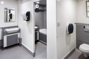A modern bathroom with a sink, mirror, towel dispenser, and toilet. - Christs College Cambridge (Cambridge)