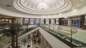 Un atrium à plusieurs niveaux, agrémenté d’un imposant lustre, de palmiers et d’un espace central ouvert avec des sièges.
