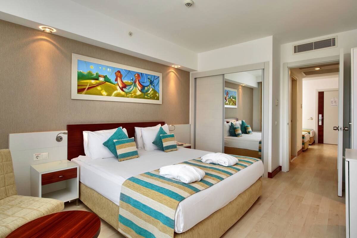 A hotel room with a large bed, a bedside table, a chair, a painting on the wall, and a mirror.
