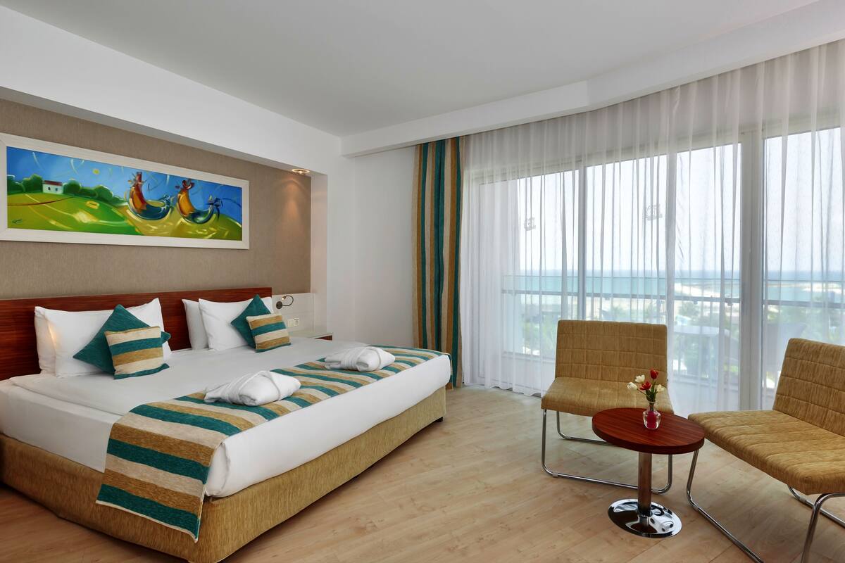 A hotel room with a large bed, two chairs, a small table, and a painting on the wall.