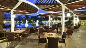 Un espacio exterior para comer con mesas y sillas, una piscina y sombrillas.