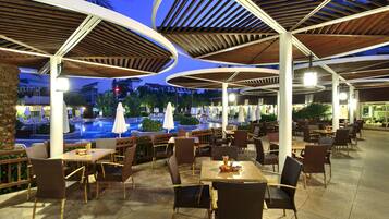 An outdoor dining area with tables and chairs, a pool, and umbrellas.