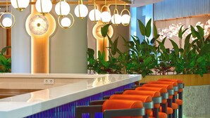Una zona de bar con una barra alargada, varias lámparas colgantes y una fila de taburetes naranjas.