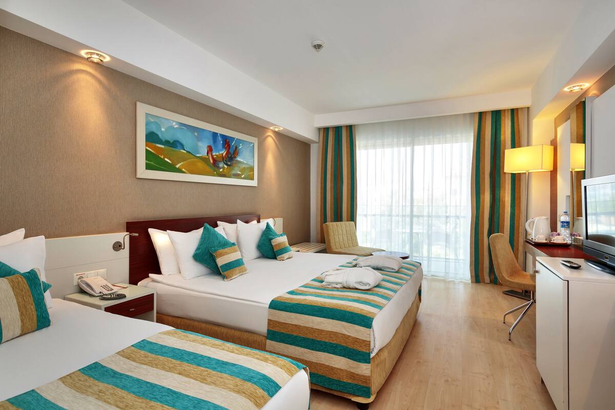 A hotel room with two beds, a desk, a chair, a TV, and a painting on the wall.