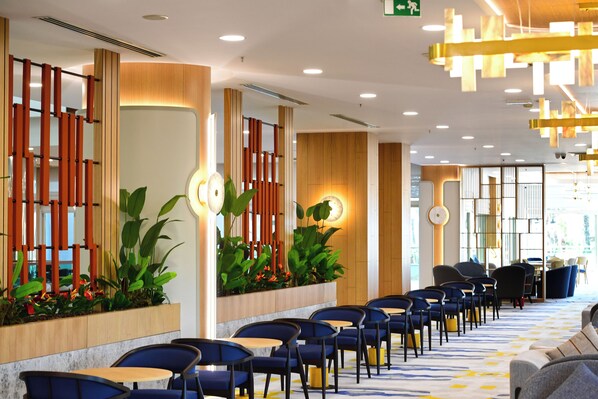 A hotel lobby with a row of tables and chairs, wooden paneling, and potted plants.