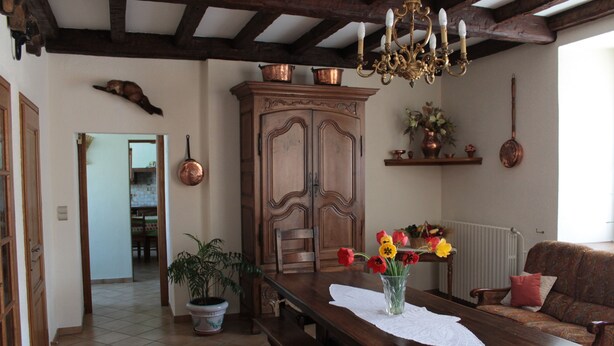 A dining area with a wooden table, benches, a vase with flowers, a chandelier, and a cabinet with copper pots.