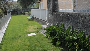 A backyard with a lawn, a white chair, and a stone wall.