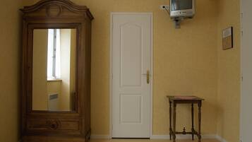 Una habitación con un amplio armario de madera, una puerta blanca, una pequeña mesa de madera y un televisor montado.