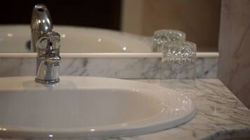 Un lavabo de salle de bain doté d’un robinet moderne, d’un plan de toilette en marbre et d’un miroir qui reflète un verre d’eau.