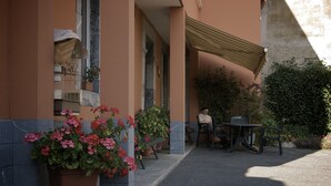 A building with a covered outdoor seating area, potted plants, and a window with a birdcage.