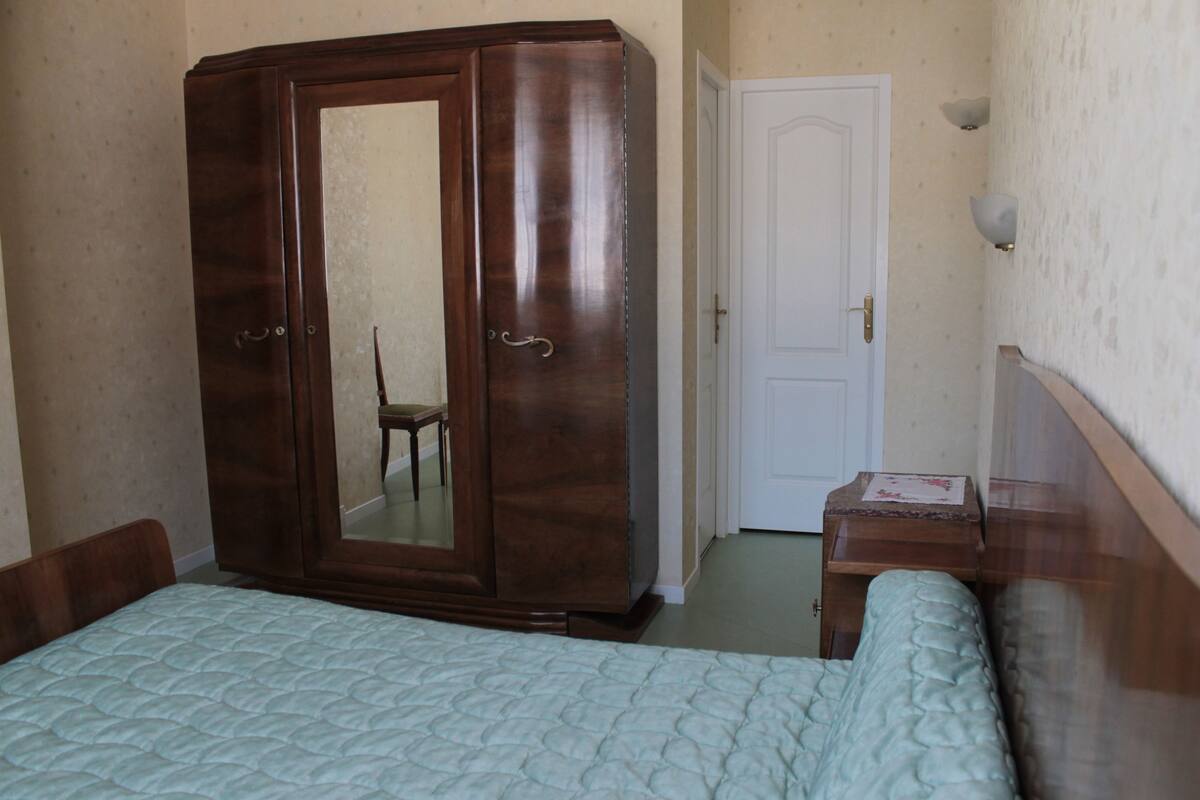 A bedroom with a bed, a wardrobe, a chair, and a door.