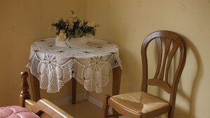 A room with a wooden chair, a table with a lace tablecloth, and a vase with flowers.
