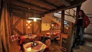 A rustic dining area with wooden walls and tables set for two, featuring checkered tablecloths and candles. - Garnì Ladin (San Giovanni di Fassa)