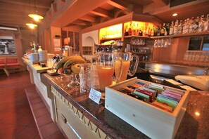 A bar area with a counter displaying various items like a pitcher of orange juice, a banana, and a tray of colorful pens. - Garnì Ladin (San Giovanni di Fassa)