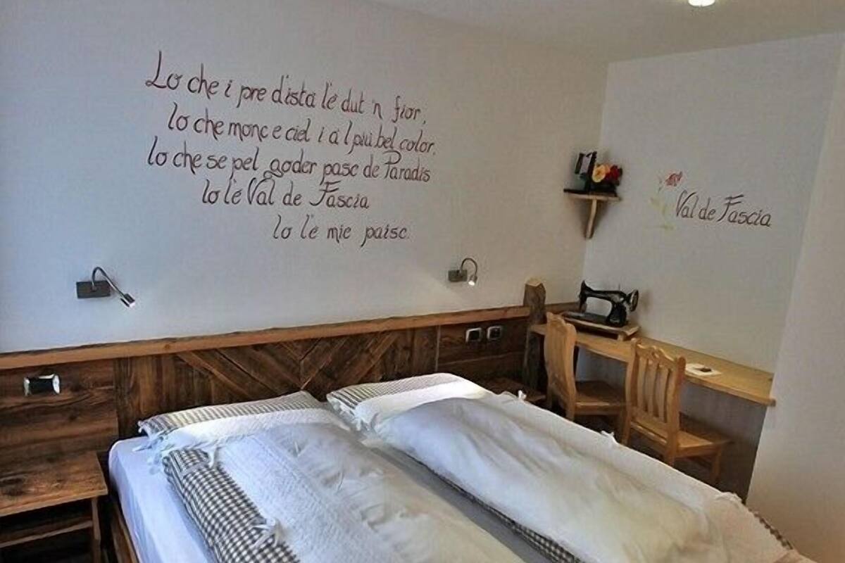 Un dormitorio con una cama de madera, un escritorio y una silla. Hay una pared con texto en un idioma extranjero.