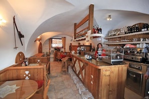 A rustic restaurant with wooden furniture, a bar area, and a kitchen. - Garnì Ladin (San Giovanni di Fassa)