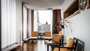 A modern hotel room with a large window, a sofa, two armchairs, a small table, and a clock on the wall. - AMERON Hamburg Hotel Speicherstadt (Hamburg)