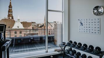 A room with a large window overlooking a cityscape, a wall clock, and a rack of dumbbells.