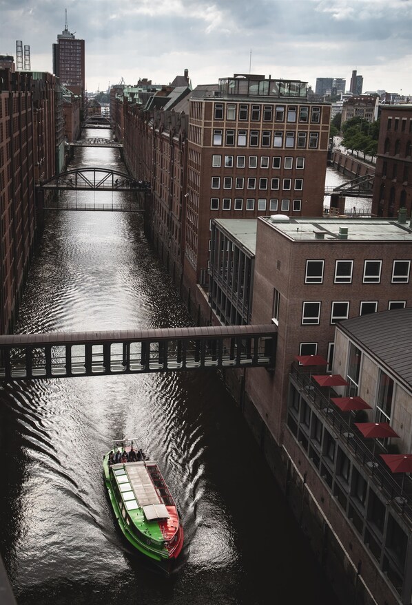 A green boat on a canal with buildings on either side. - AMERON Hamburg Hotel Speicherstadt (Hamburg)