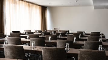 A conference room with rows of tables and chairs, equipped with water pitchers, in a modern hotel setting.