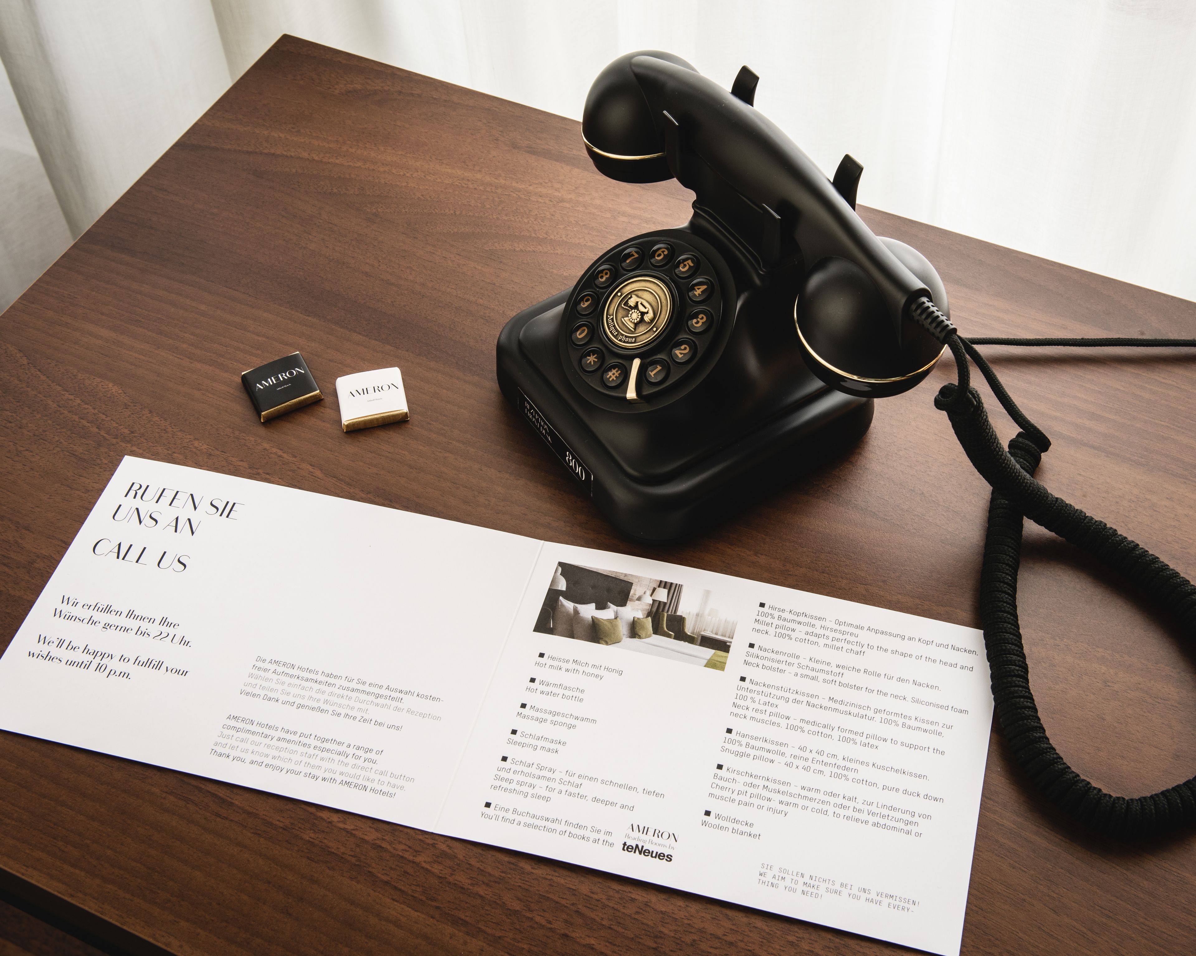 A vintage black telephone on a wooden table with a brochure and a small box labeled "AMERON".