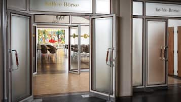 A modern interior with a coffee bar named "Kaffee-Börse," featuring glass doors, a wooden floor, and a stained glass window in the background.