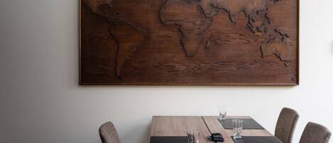 A wooden world map artwork on a wall above a wooden dining table with chairs.