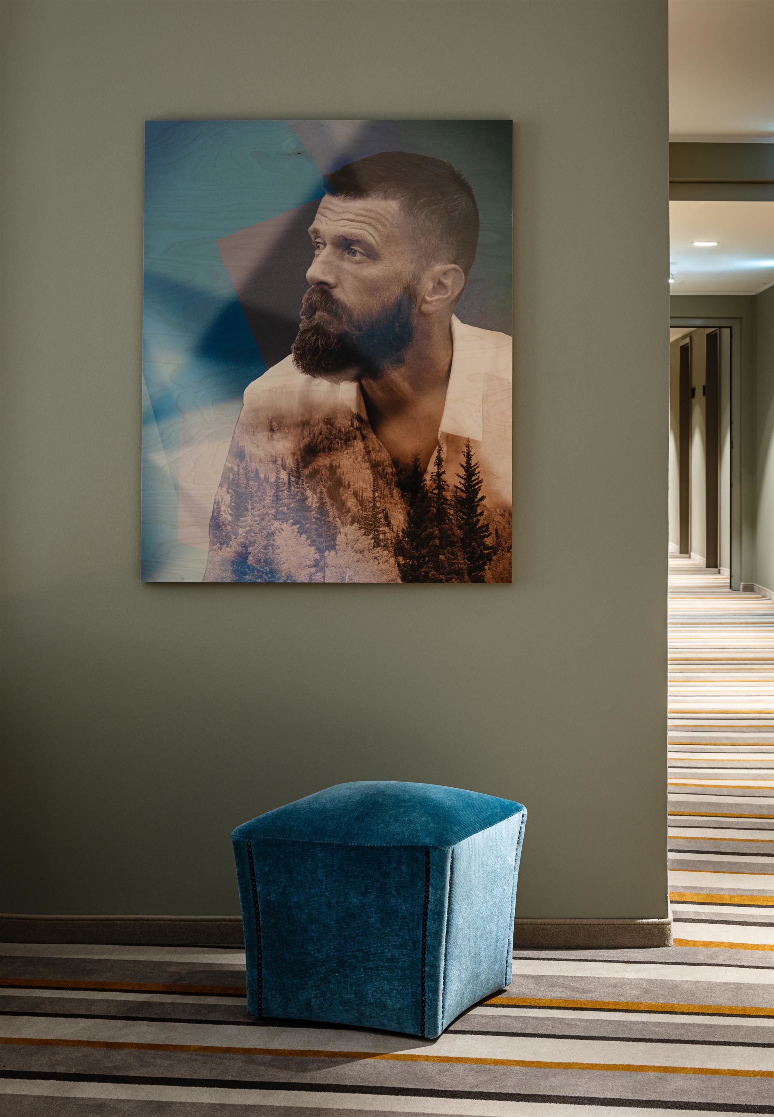 A room with a large framed artwork on the wall, a blue upholstered bench, and a striped carpet.