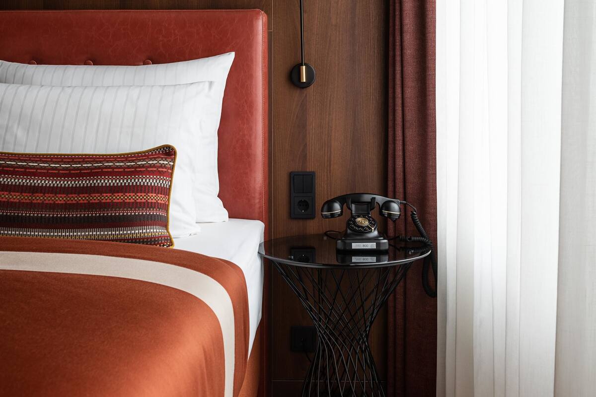 A hotel room with a bed, a desk with a telephone, and a lamp.